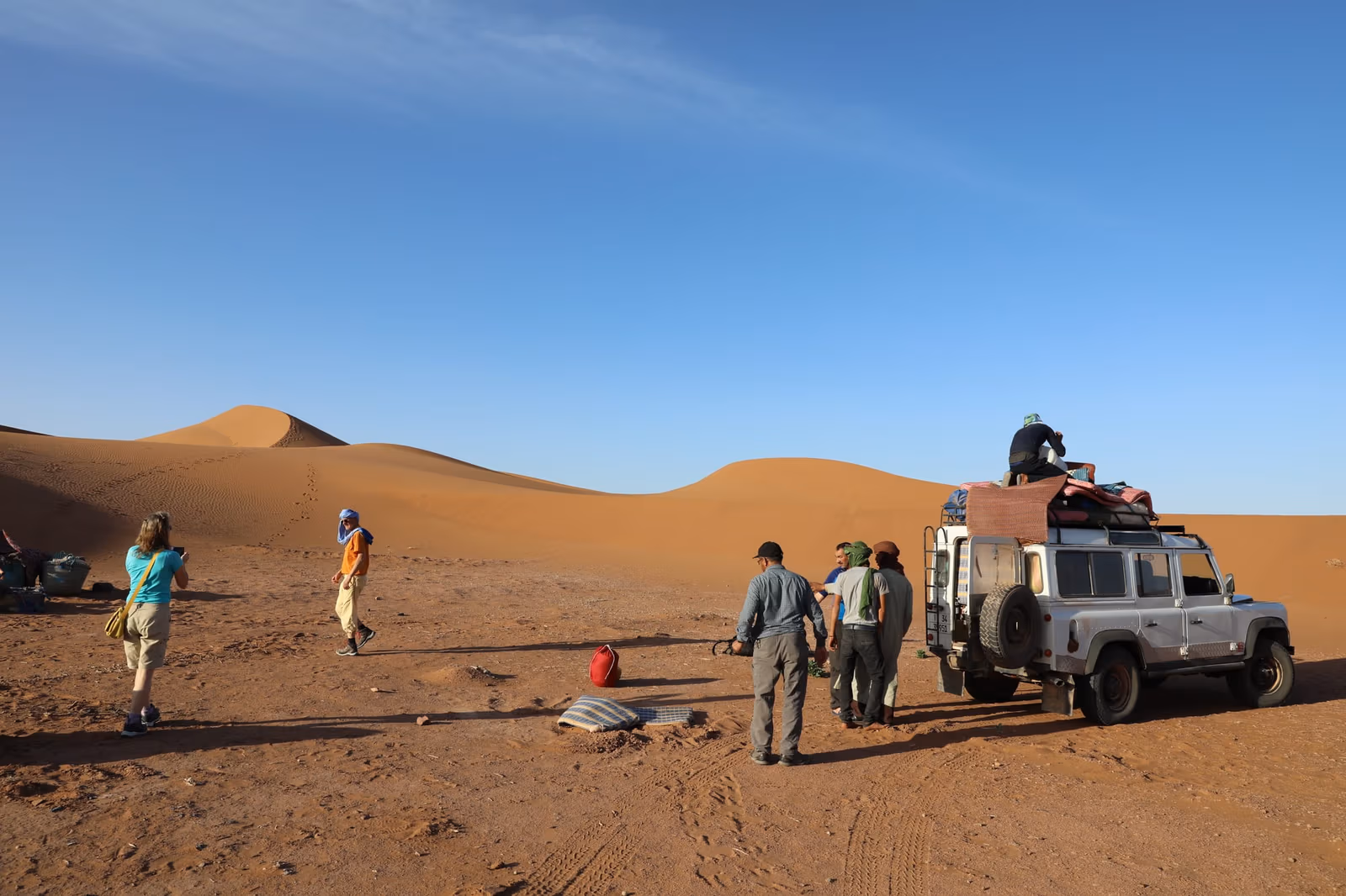 A 4×4 being unloaded on a desert track at the edge of the dunes